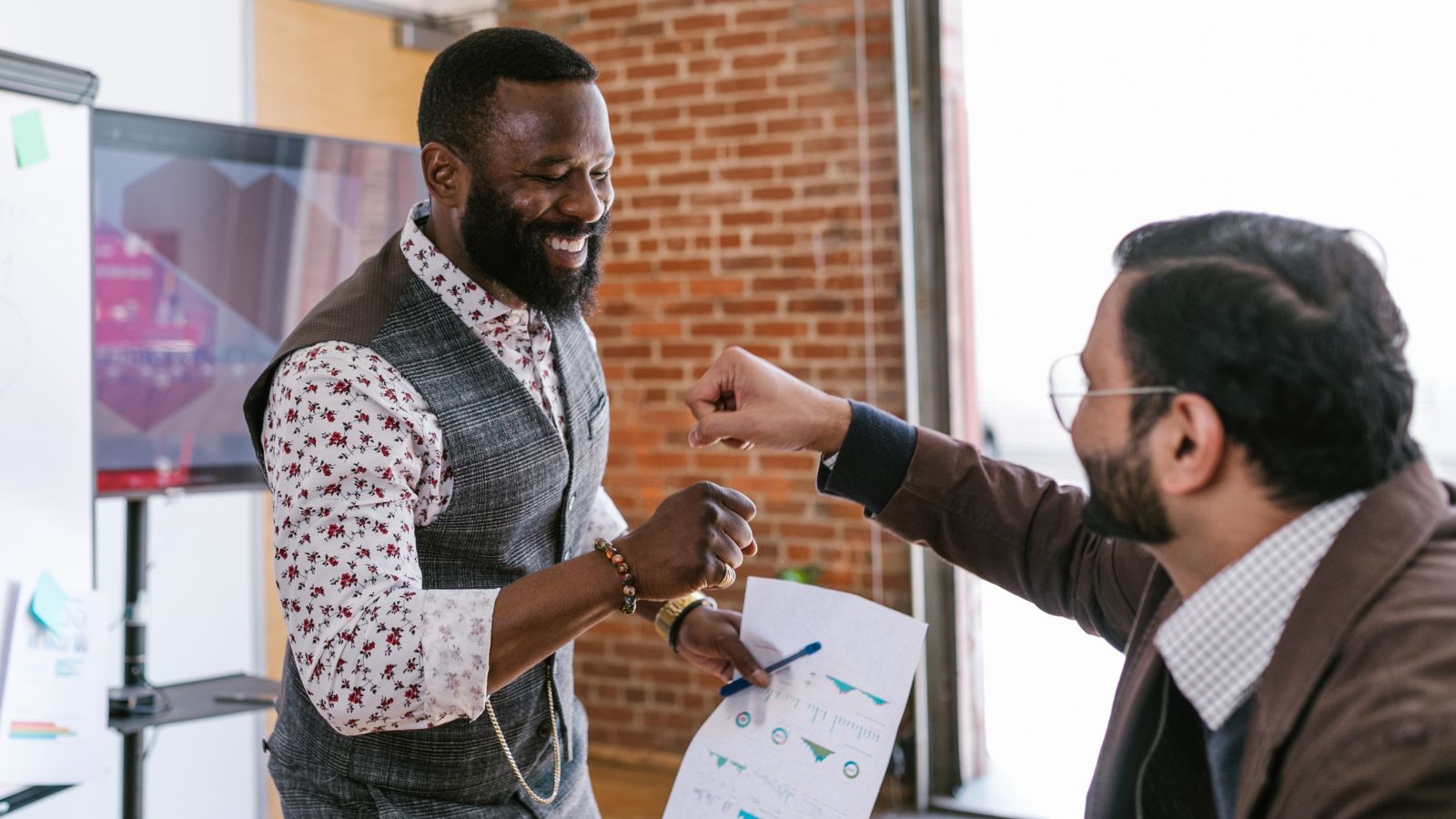 Two men in an office talking happily and having a fist bump