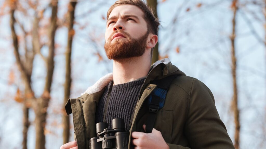 Bearded man wearing a backpack gazing out while in the woods