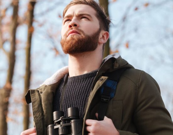 Bearded man wearing a backpack gazing out while in the woods