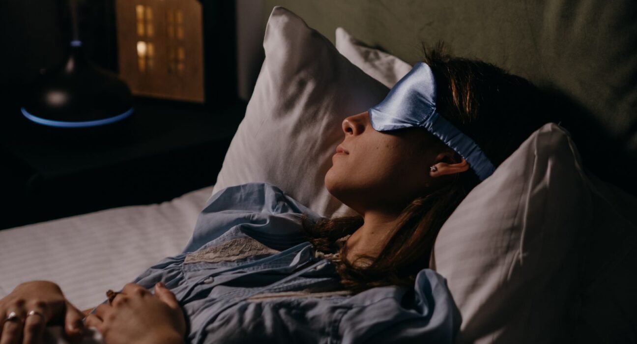 A woman trying to have a good night's sleep by using a sleeping eye mask to protect her eyes from bright light