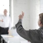 Male employee raising hand to ask a question in the office boardroom