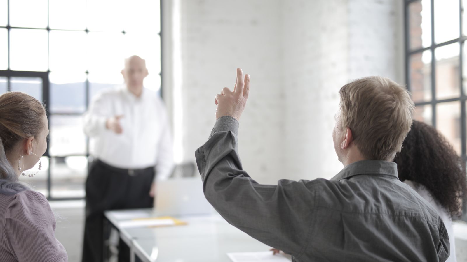 Male employee raising hand to ask a question in the office boardroom