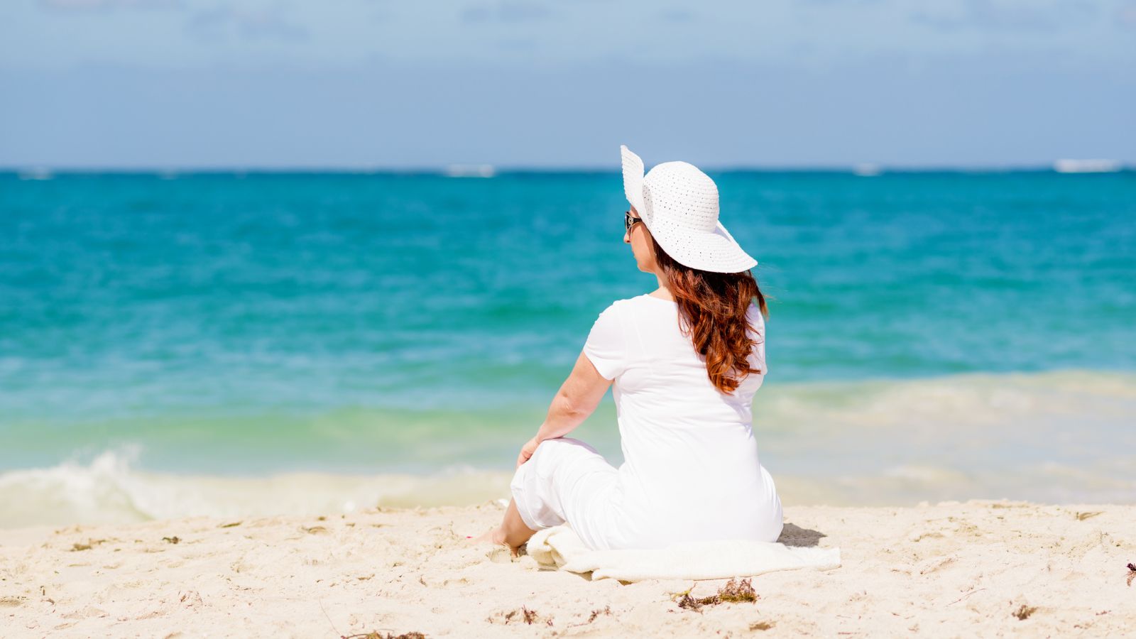 A woman sitting upright on the beach enjoying the ocean view