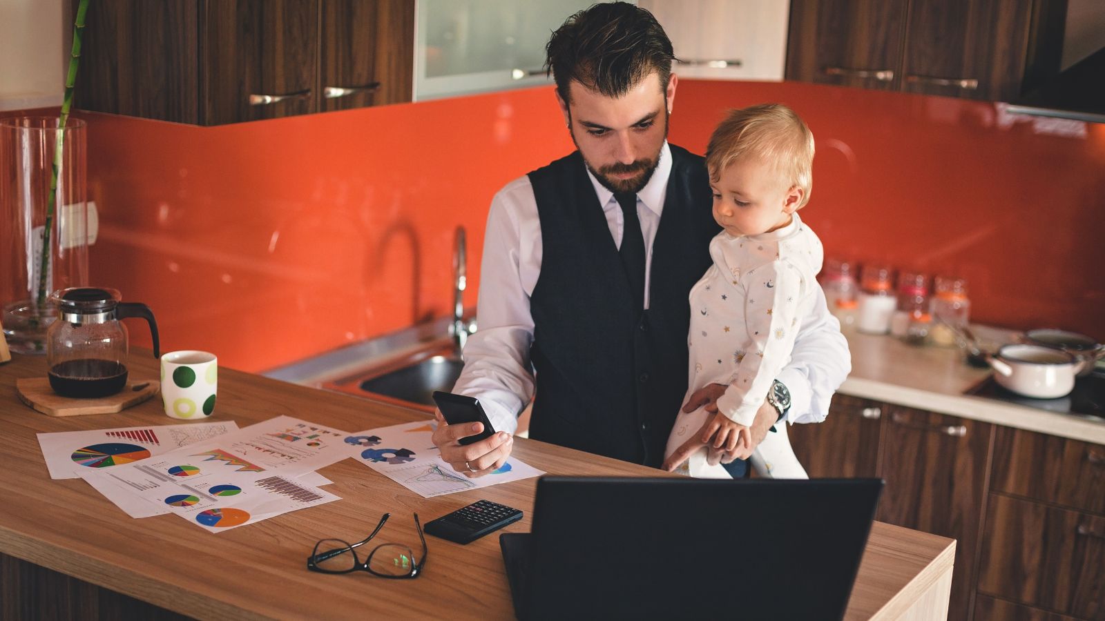 Working father holding a baby boy while working in the kitchen